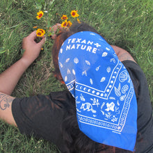 Person wearing a blue bandana with 'Texan Nature' text, lying on grass and picking flowers.