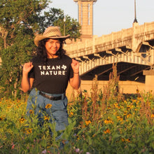 Person wearing a 'Texas Nature' t-shirt in a field with a bridge and trees in the background